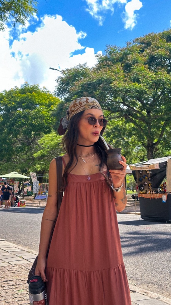 Carol de vestido terracota e lenço na cabeça, em uma feira ao ar livre